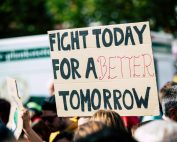 Crowd holding a protest sign with 'Fight Today for a Better Tomorrow', outdoors and during the day.