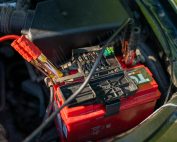 Close-up view of a car battery with red jumper cables connected, outdoors.
