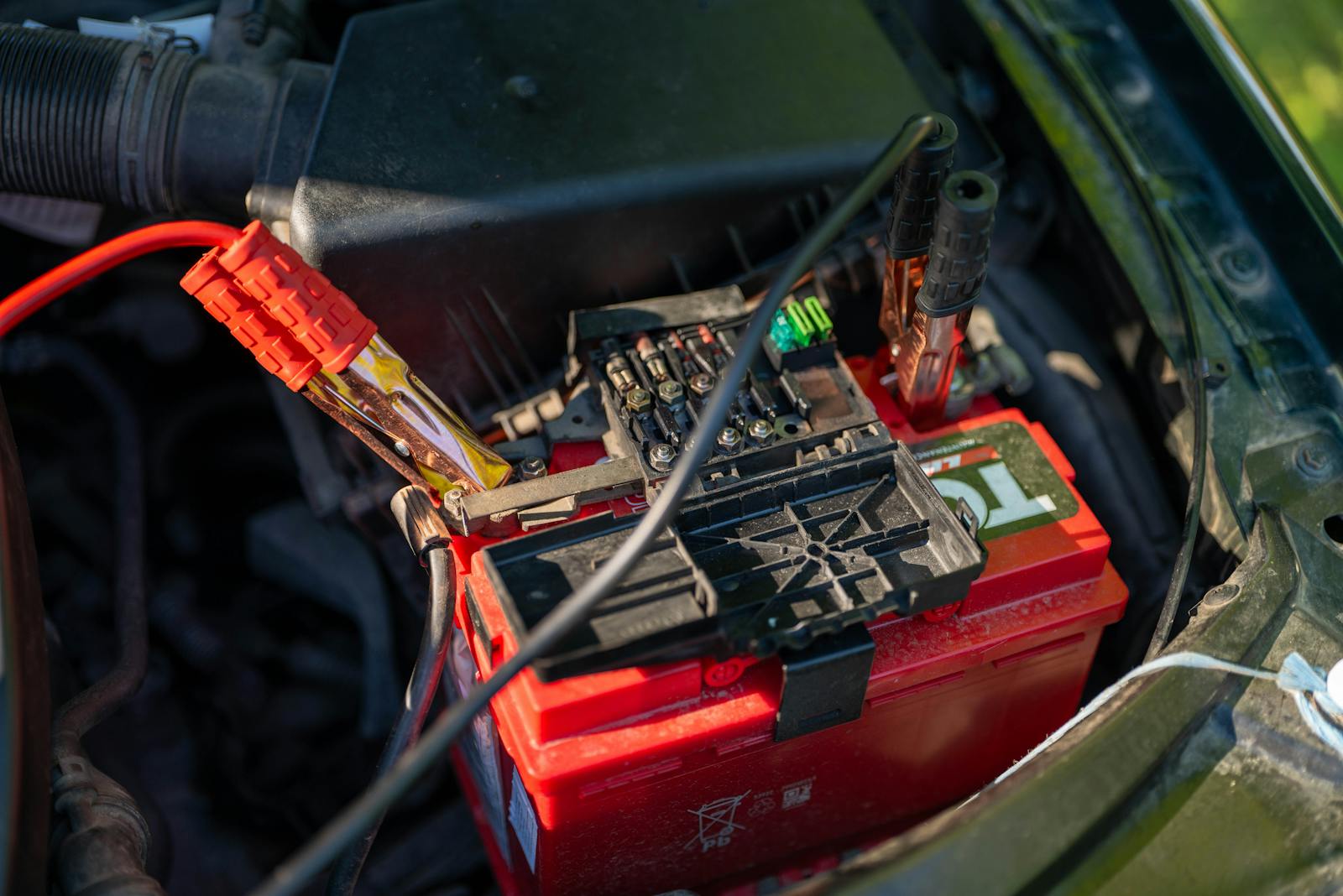 Close-up view of a car battery with red jumper cables connected, outdoors.