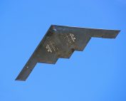 A B-2 stealth bomber from the US Air Force flying against a clear blue sky.