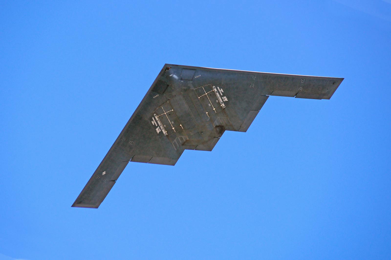 A B-2 stealth bomber from the US Air Force flying against a clear blue sky.
