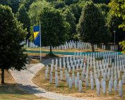 A solemn view of the Srebrenica Memorial, featuring rows of white gravestones and the Bosnian flag.