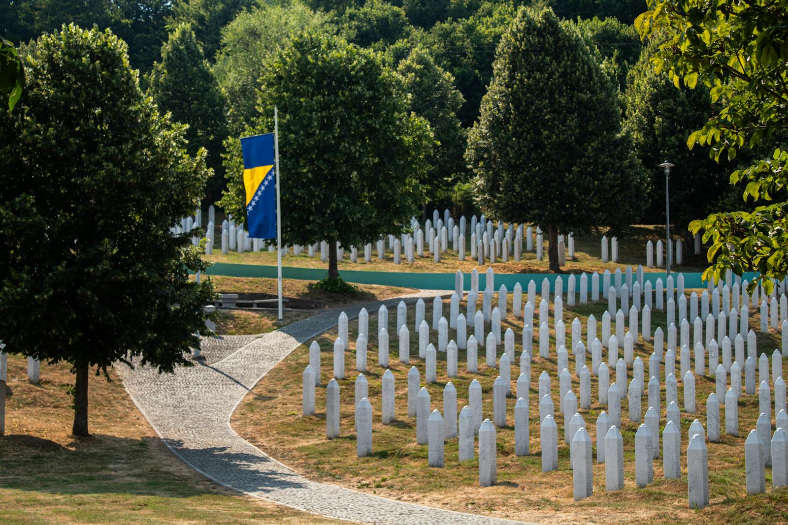 A solemn view of the Srebrenica Memorial, featuring rows of white gravestones and the Bosnian flag.