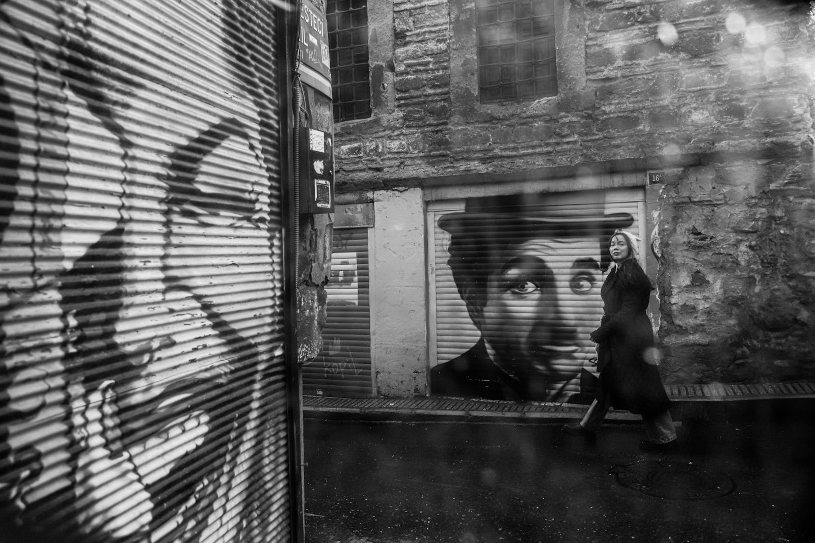 Black and white street art scene capturing a woman walking by iconic mural in İstanbul.