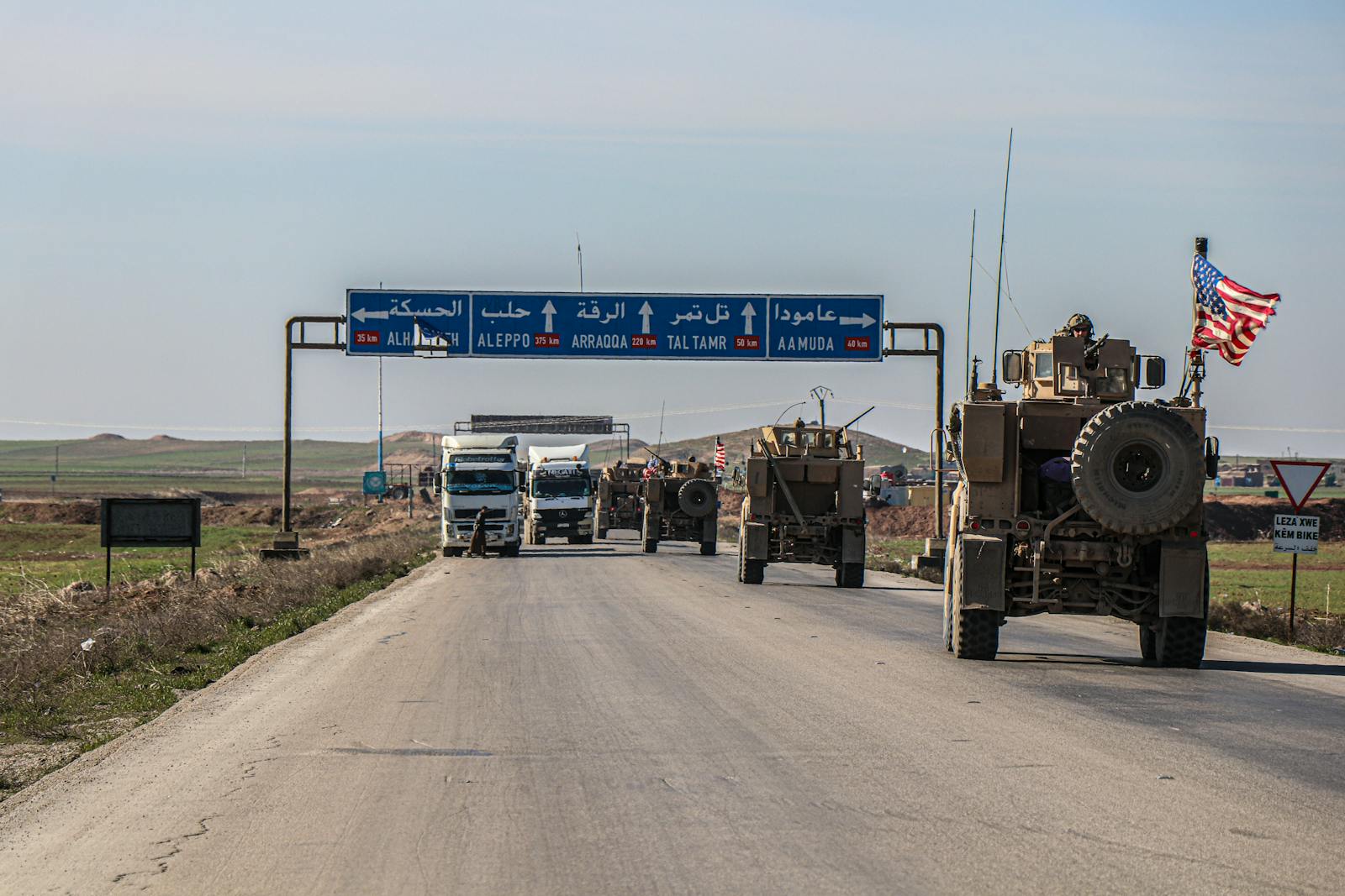 US military convoy travels on a highway in Al Hasakah, Syria, under blue skies.