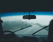 Interior car view on a rainy day with water droplets on windshield and wipers in motion.