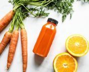 Carrot and orange juice with fresh carrots and sliced orange on a white background.