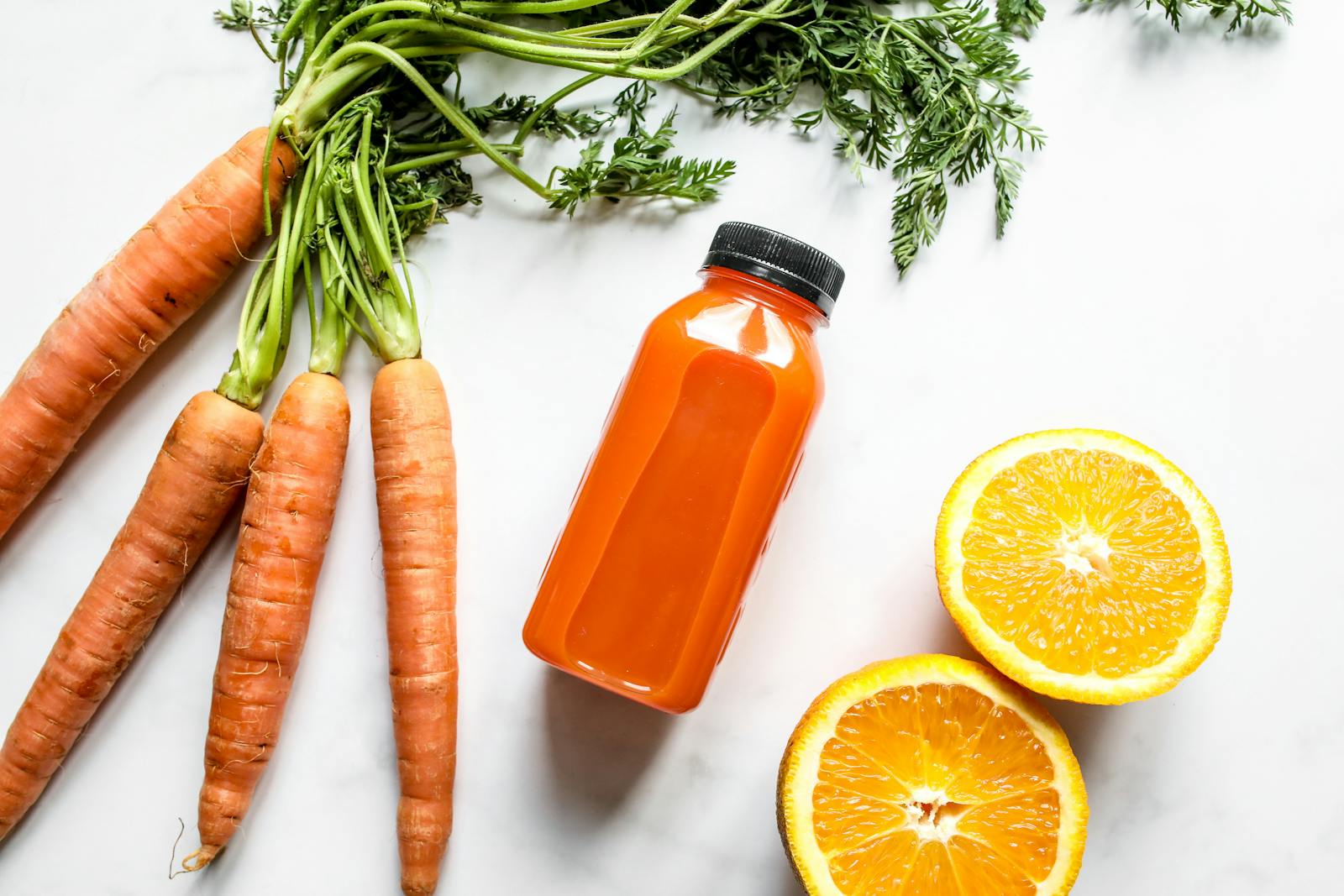Carrot and orange juice with fresh carrots and sliced orange on a white background.