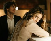 A stylish man and woman share a moment at a bar, with warm ambient lighting.