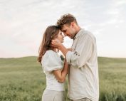A loving couple embraces in a picturesque field during sunset, capturing a romantic moment.