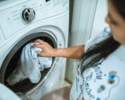 A woman loading laundry into a washing machine indoors, focusing on household chores.