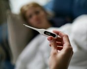 Hand holding a digital thermometer with blurred background of a sick person.