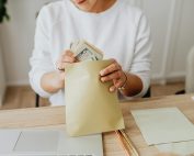 Close-up of person holding envelopes with cash at a wooden desk indoors.