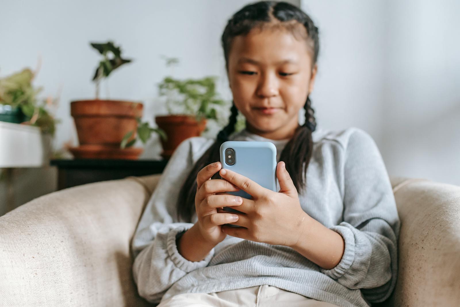 A young girl comfortably using her smartphone indoors, surrounded by plants.