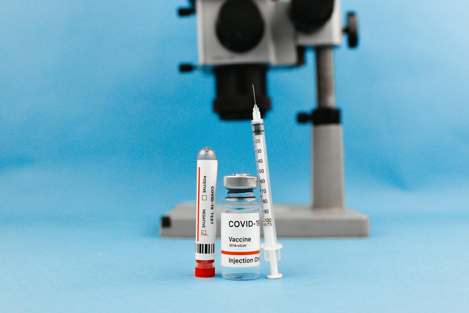 COVID-19 vaccine vial, syringe, test tube, and microscope on blue background, symbolizing research and healthcare.