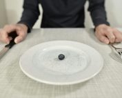 A single blueberry on a scratched plate symbolizes minimalist diet and portion control.