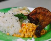 Close-up of a flavorful chicken dish with rice, corn, and an egg on a green plate.