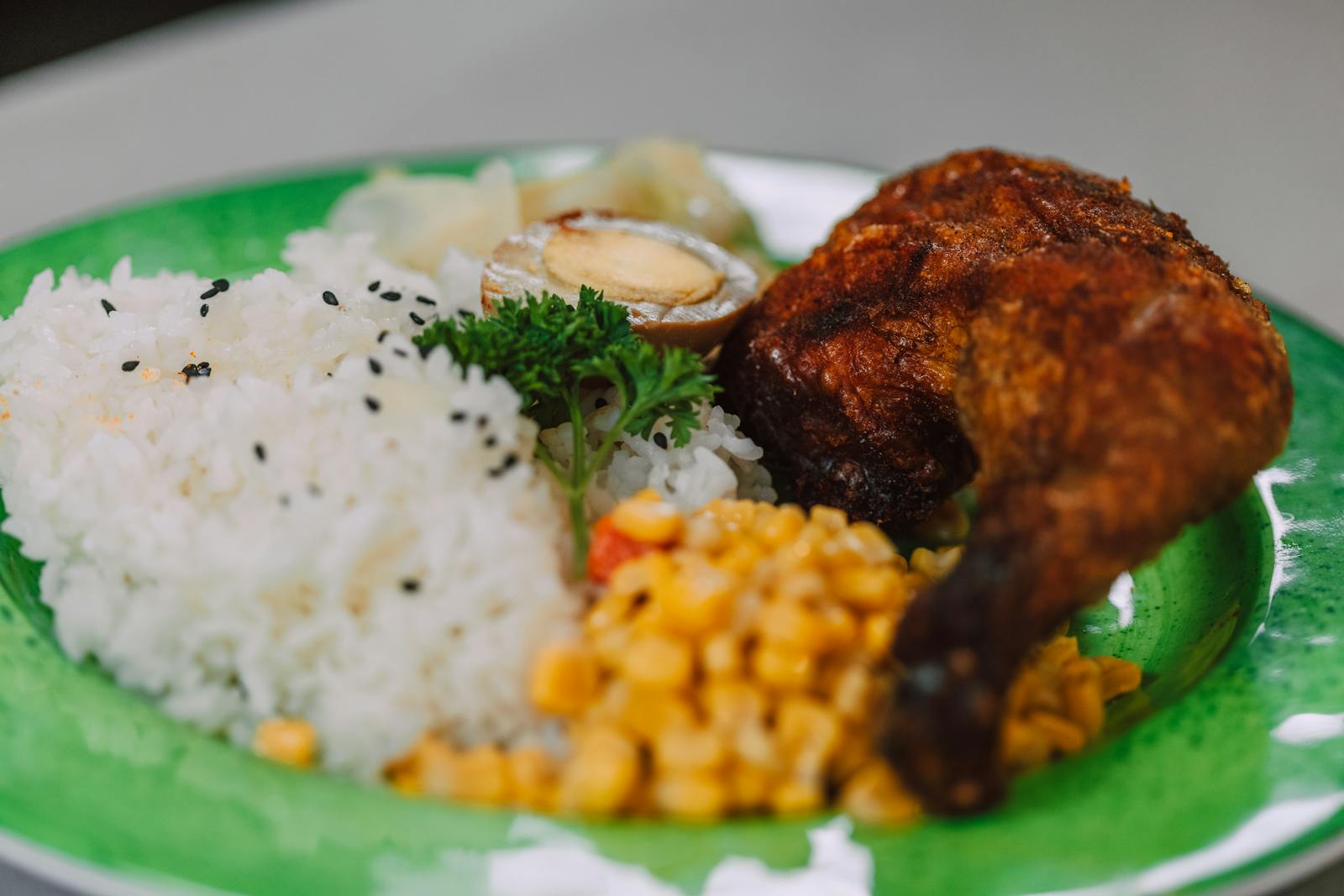 Close-up of a flavorful chicken dish with rice, corn, and an egg on a green plate.