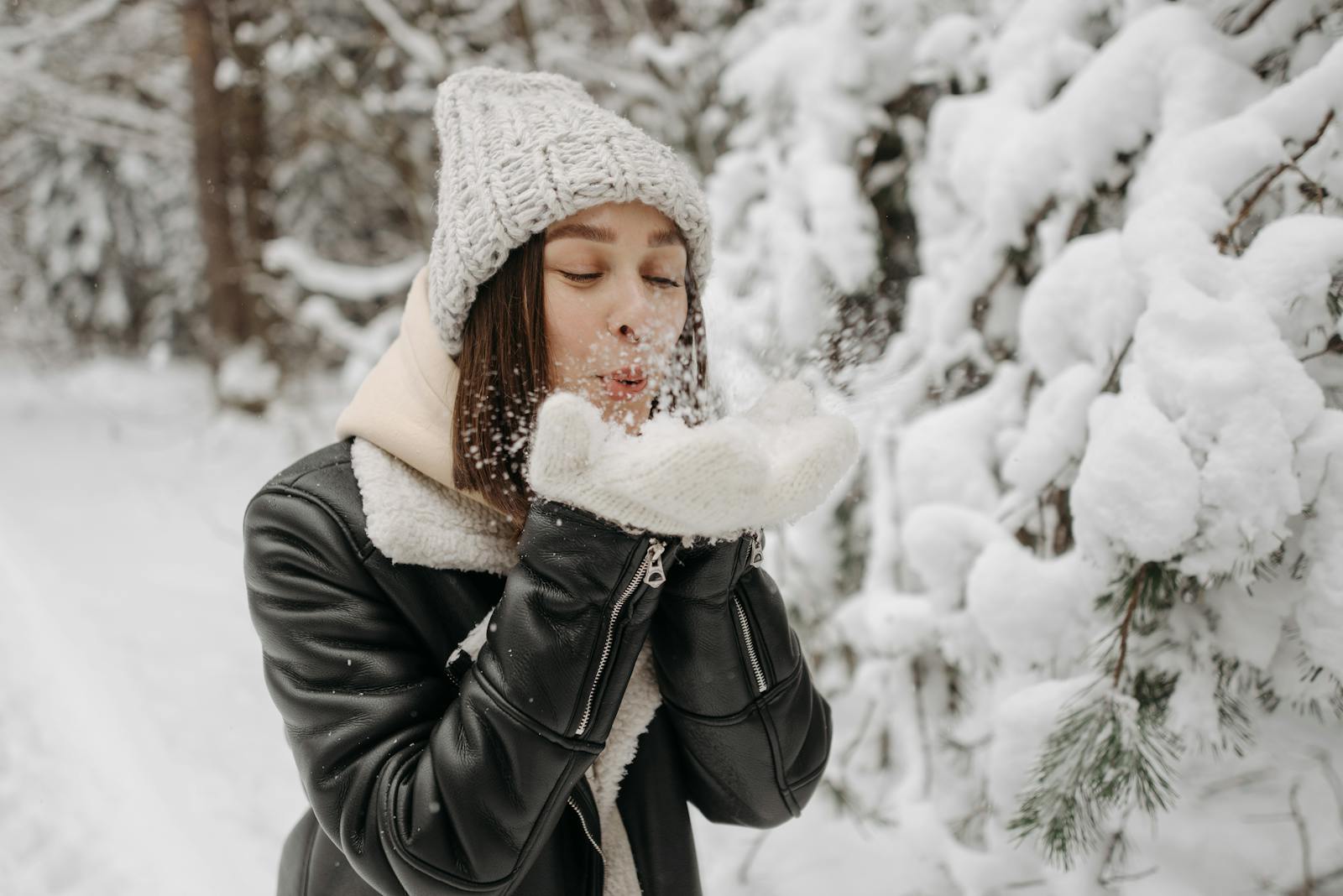 Caucasian woman blowing snow in a winter forest, wearing warm clothes.