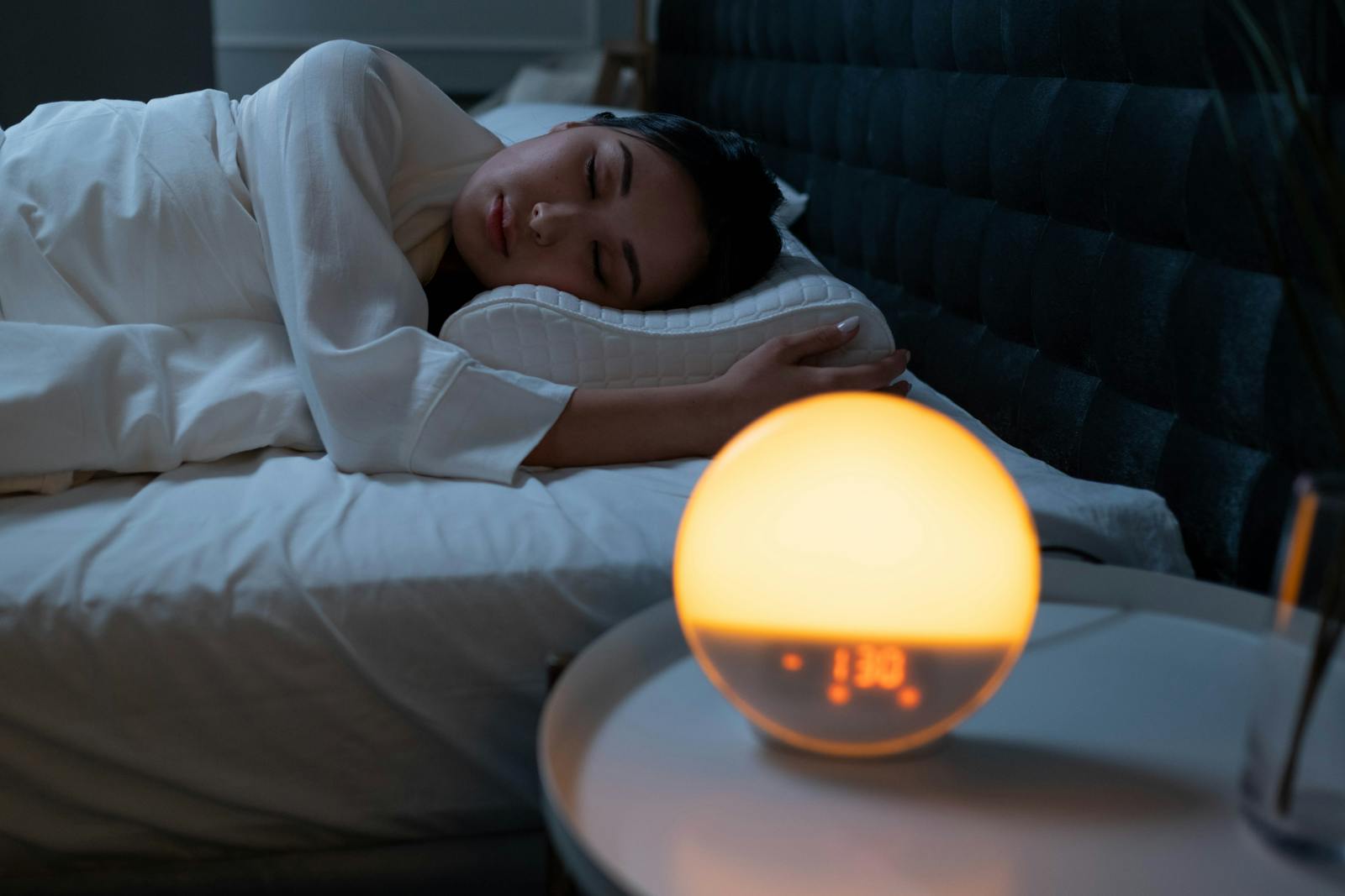 Woman sleeping peacefully in a cozy bedroom with ambient bedside light.