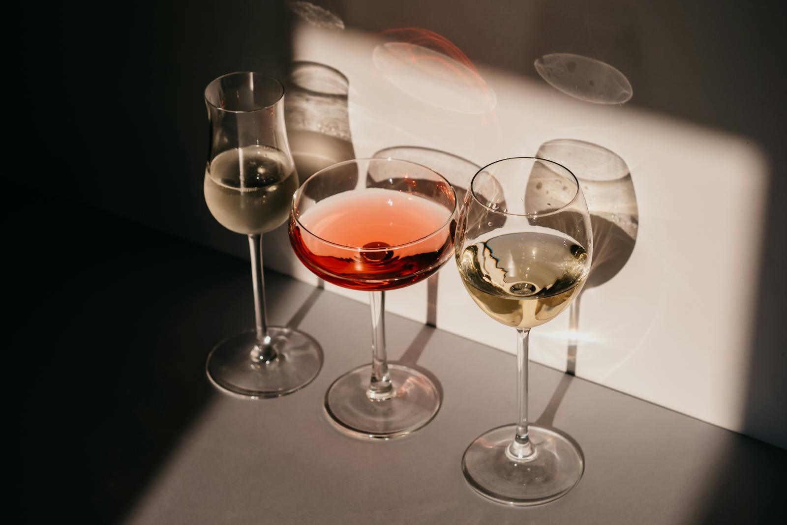Elegant arrangement of three wine glasses casting distinct shadows in warm light.