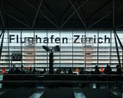 Travelers waiting at Zürich Airport with silhouettes against modern architecture.
