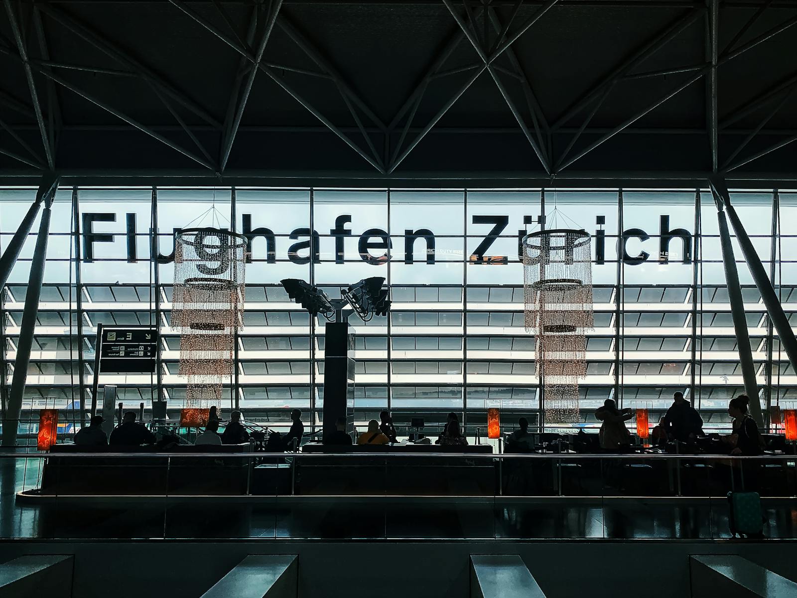 Travelers waiting at Zürich Airport with silhouettes against modern architecture.