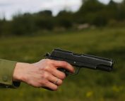 A close-up of a hand wearing a silver ring, holding a pistol outdoors.