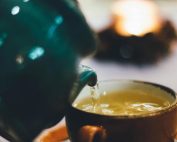Warm close-up image of tea being poured into a teacup with blurred background ambiance.