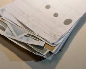 Close-up view of a stack of various papers and documents on a desk surface.