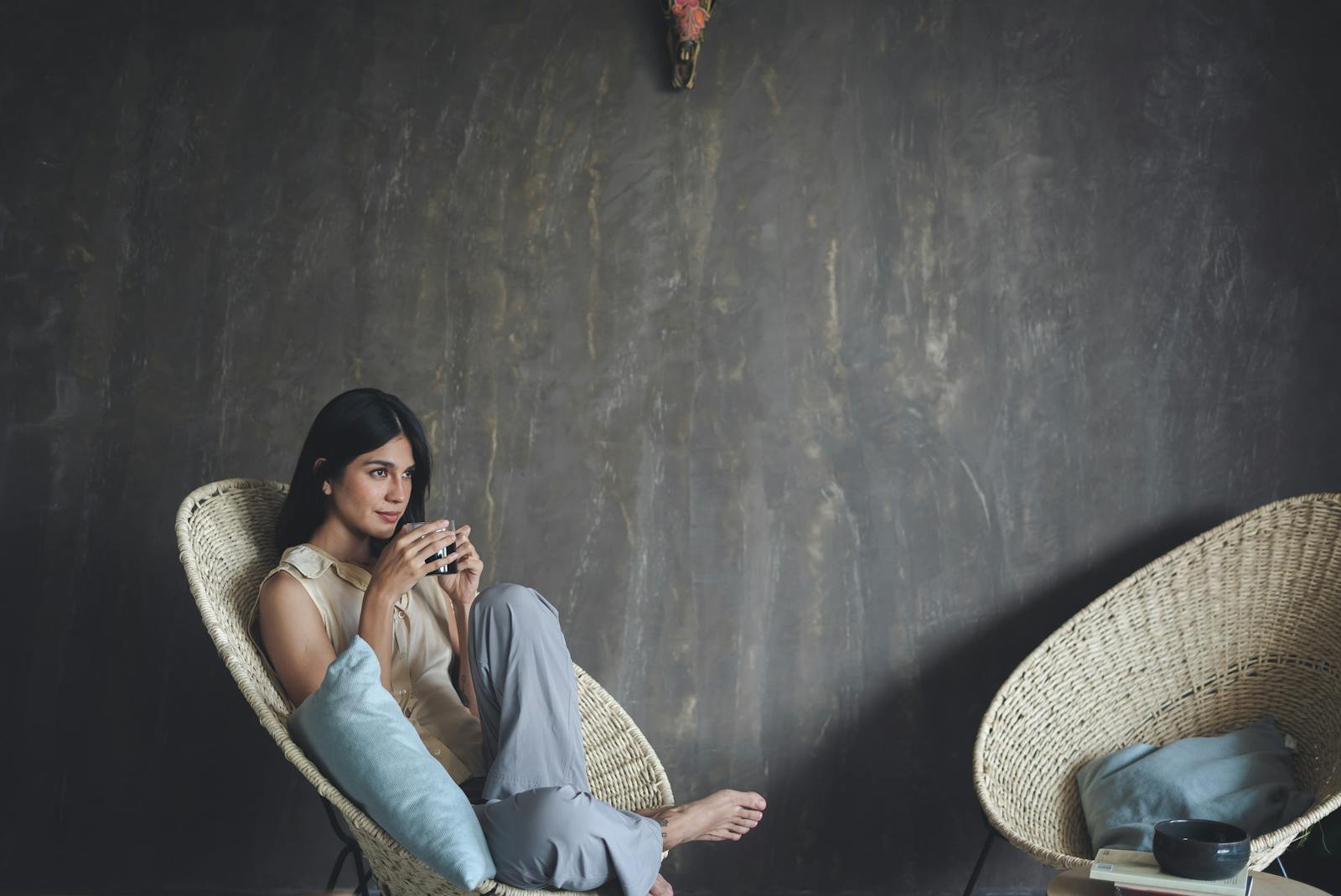 Woman sitting comfortably with a hot drink in a modern, minimalist setting.