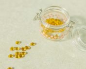 Close-up of open glass jar filled with yellow health capsules on light surface.