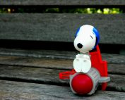 Playful Snoopy plastic toy resting on a rustic wooden bench in an outdoor setting.