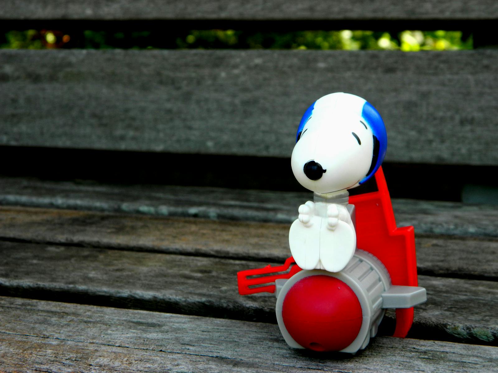 Playful Snoopy plastic toy resting on a rustic wooden bench in an outdoor setting.