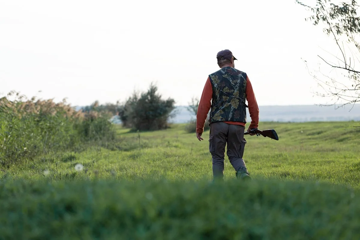 Lovac u zelenoj prirodi sa puškom preko ramena