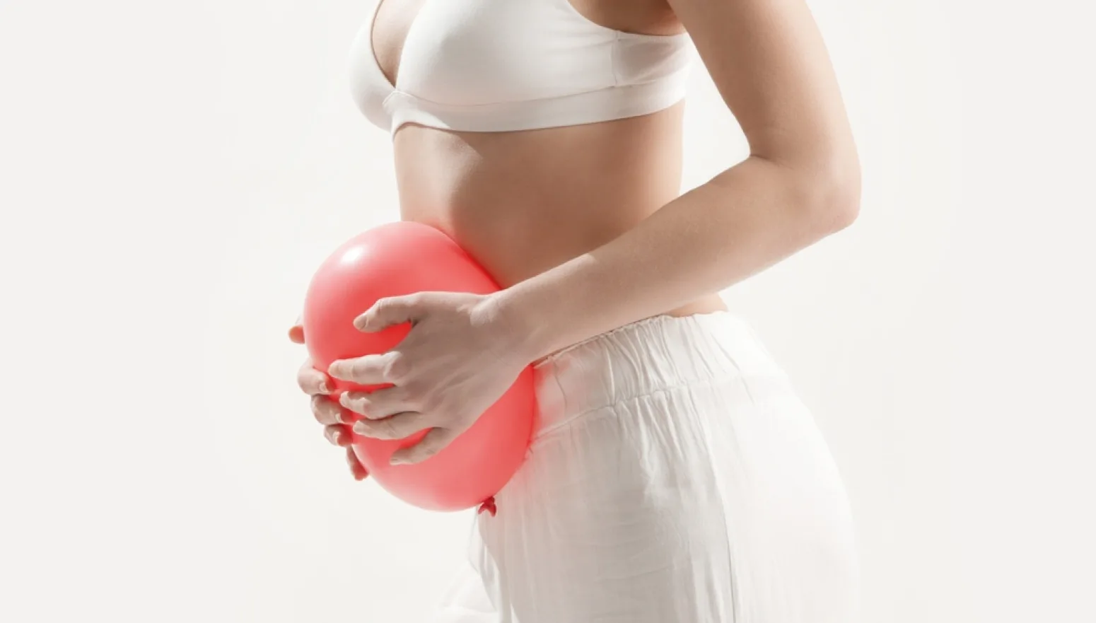 Žena drži crveni balon na stomaku, koncept trudnoće ili nadutosti.