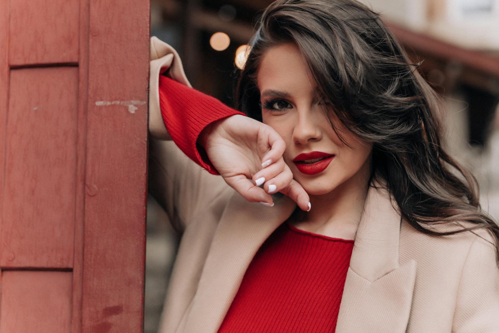 Portrait of an elegant woman with long brunette hair in a beige coat and red outfit, exuding fashion allure.