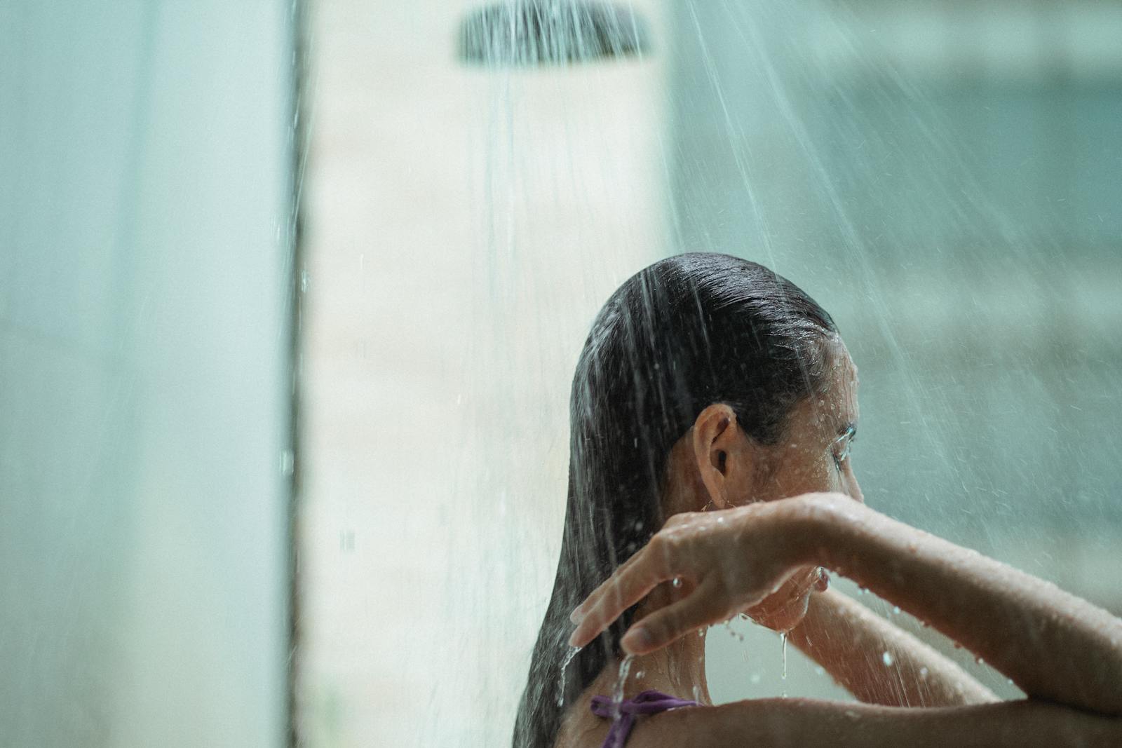 Side view of a woman with wet hair enjoying a tranquil shower, illustrating relaxation and self-care.