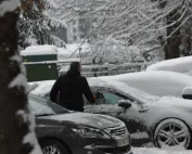 Muškarac čisti snijeg sa automobila tokom snježnog dana.