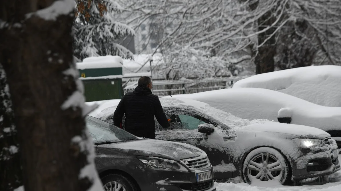 Muškarac čisti snijeg sa automobila tokom snježnog dana.