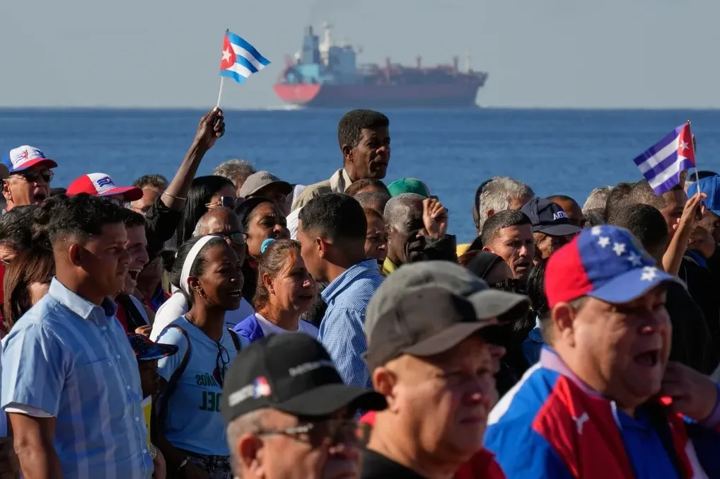Grupa ljudi protestuje sa kubanskim zastavama pored mora.