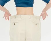 A woman's back view showcasing weight loss with oversized pants in a studio setting.