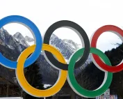 Olimpijski krugovi u bojama sa snježnim planinama u pozadini, simbolizujući Olimpijske igre.