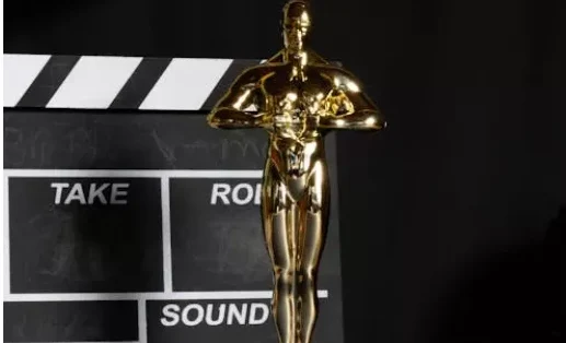 Zlatna statua Oskara s filmskom klapom u pozadini, simbol kinematografije i nagrada za filmska dostignuća.
