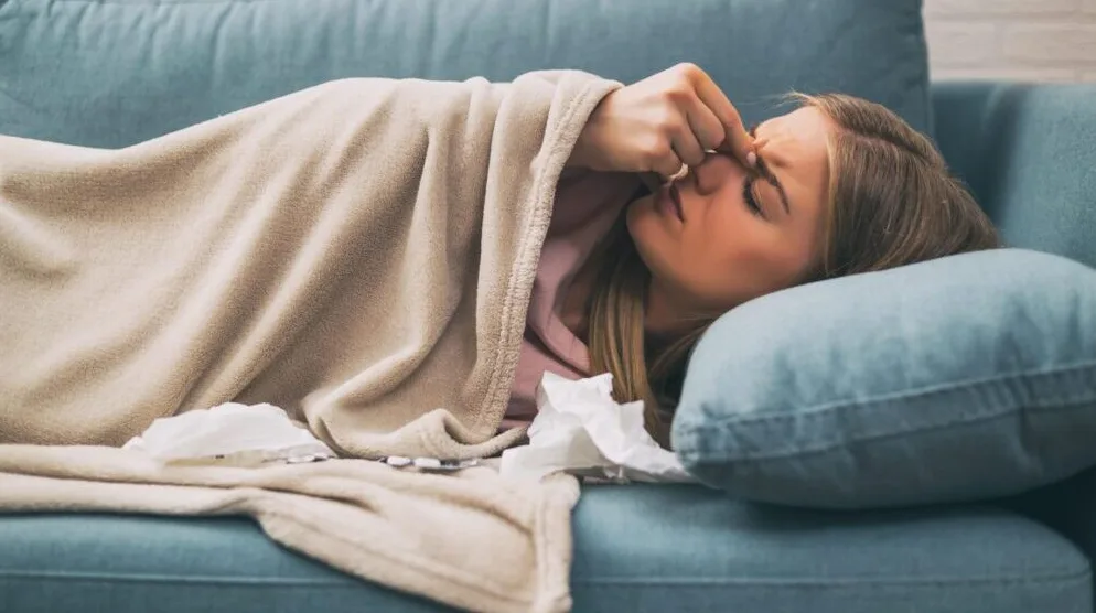 Bolesna žena leži na kauču sa temperaturom i glavoboljom.