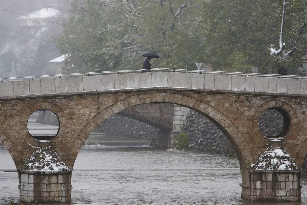 Osoba sa kišobranom prelazi kameni most u Sarajevu tokom snježnih padavina.