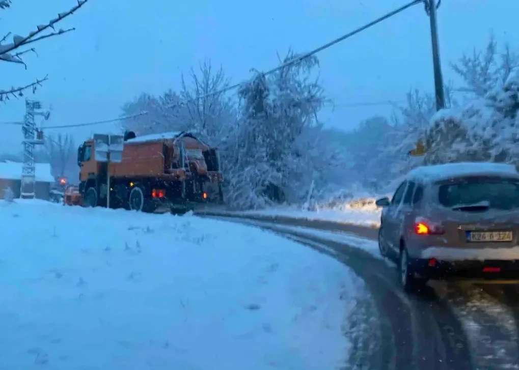 Kamion za čišćenje snijega na zaleđenom putu pored automobila.