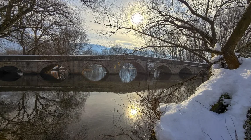 Sniježni pejzaž: Stari kameni most se ogleda u mirnoj rijeci tokom zime.