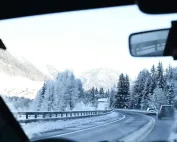 Pogled iz automobila na zimski pejzaž sa planinama i cestom prekrivenom snijegom.