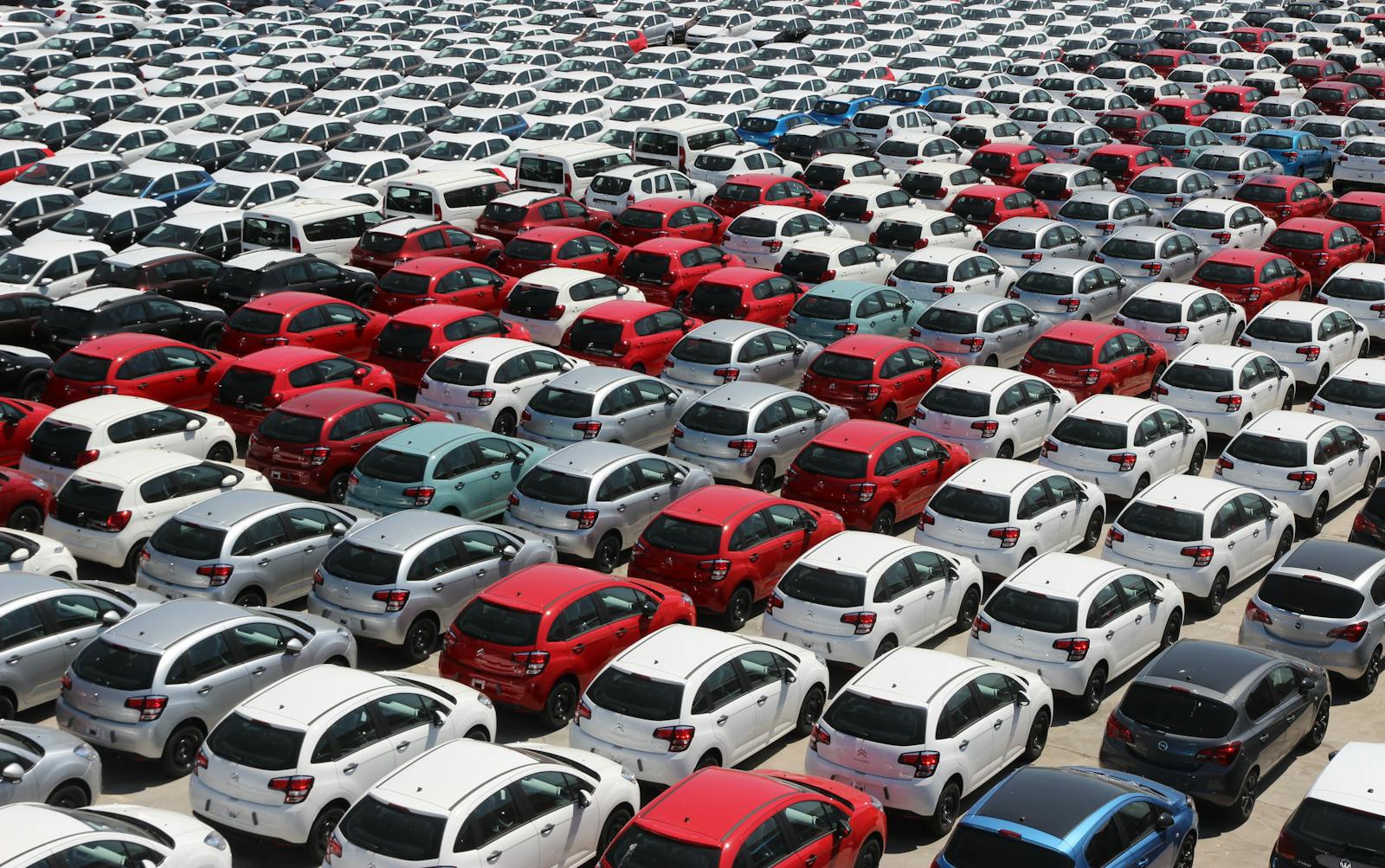 Overhead shot of neatly parked colorful cars in a large outdoor lot under sunlight.
